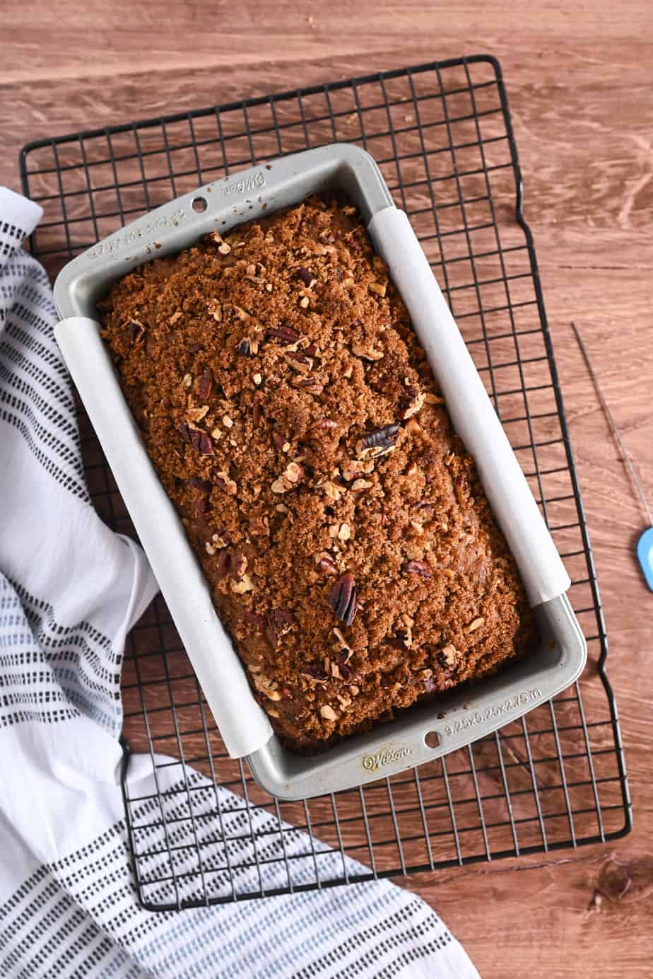 Baked loaf of applesauce bread in a loaf pan set on a wire cooling rack.