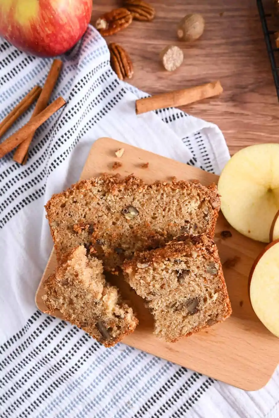 Overhead view of two slices of applesauce bread on a wooden board. One slice is broken into two pieces.