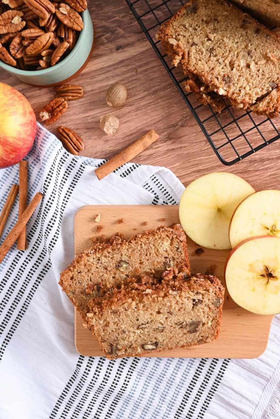 Overhead view of two slices of applesauce bread on a wooden board next to sliced apples.