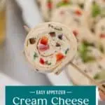 Hand holding up a cream cheese ranch roll up on a toothpick to the camera. Text overlay includes recipe name.