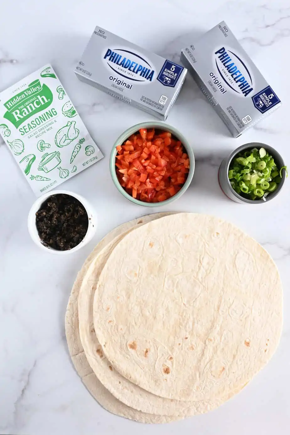 Ingredients for cream cheese ranch rollups on a marble countertop.