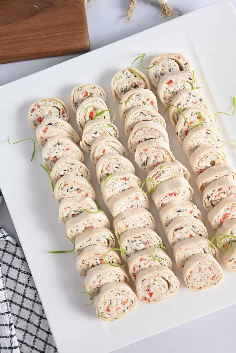 Cream cheese roll ups arranged on a white platter, set on a marble countertop.
