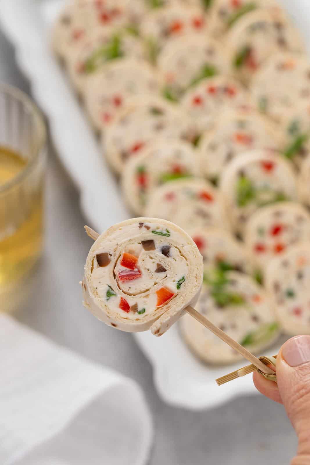 Hand holding up a cream cheese ranch roll up on a toothpick to the camera.