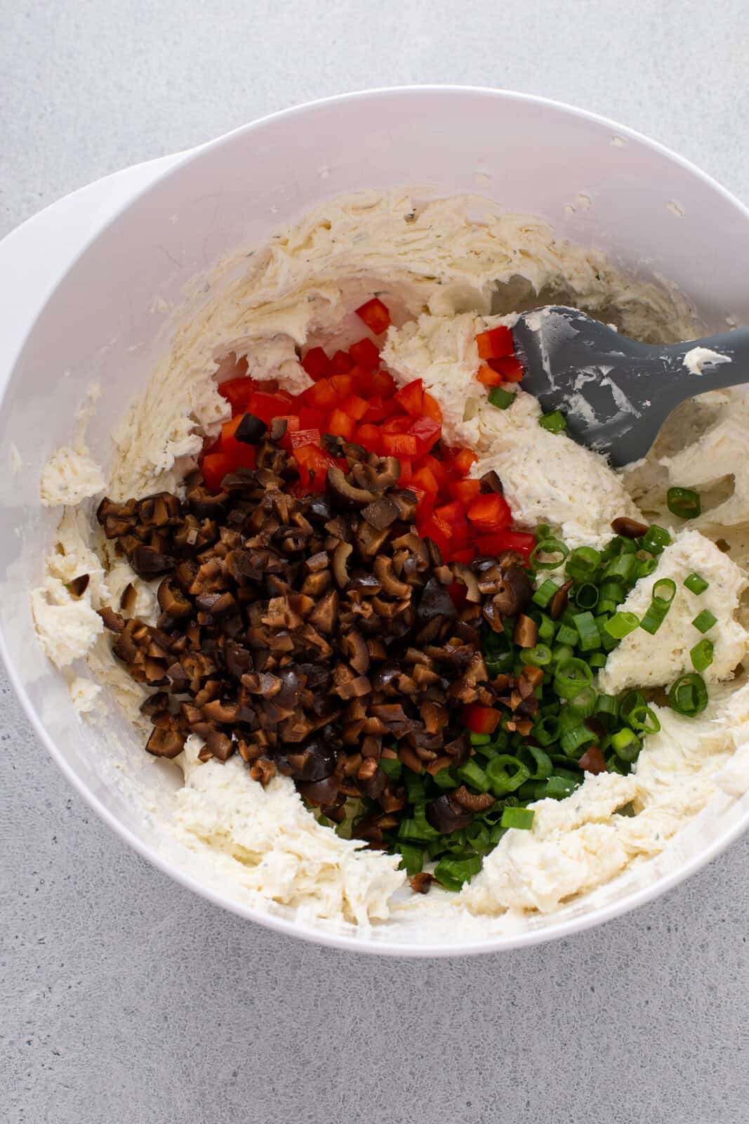Adding vegetables to cream cheese in a bowl.