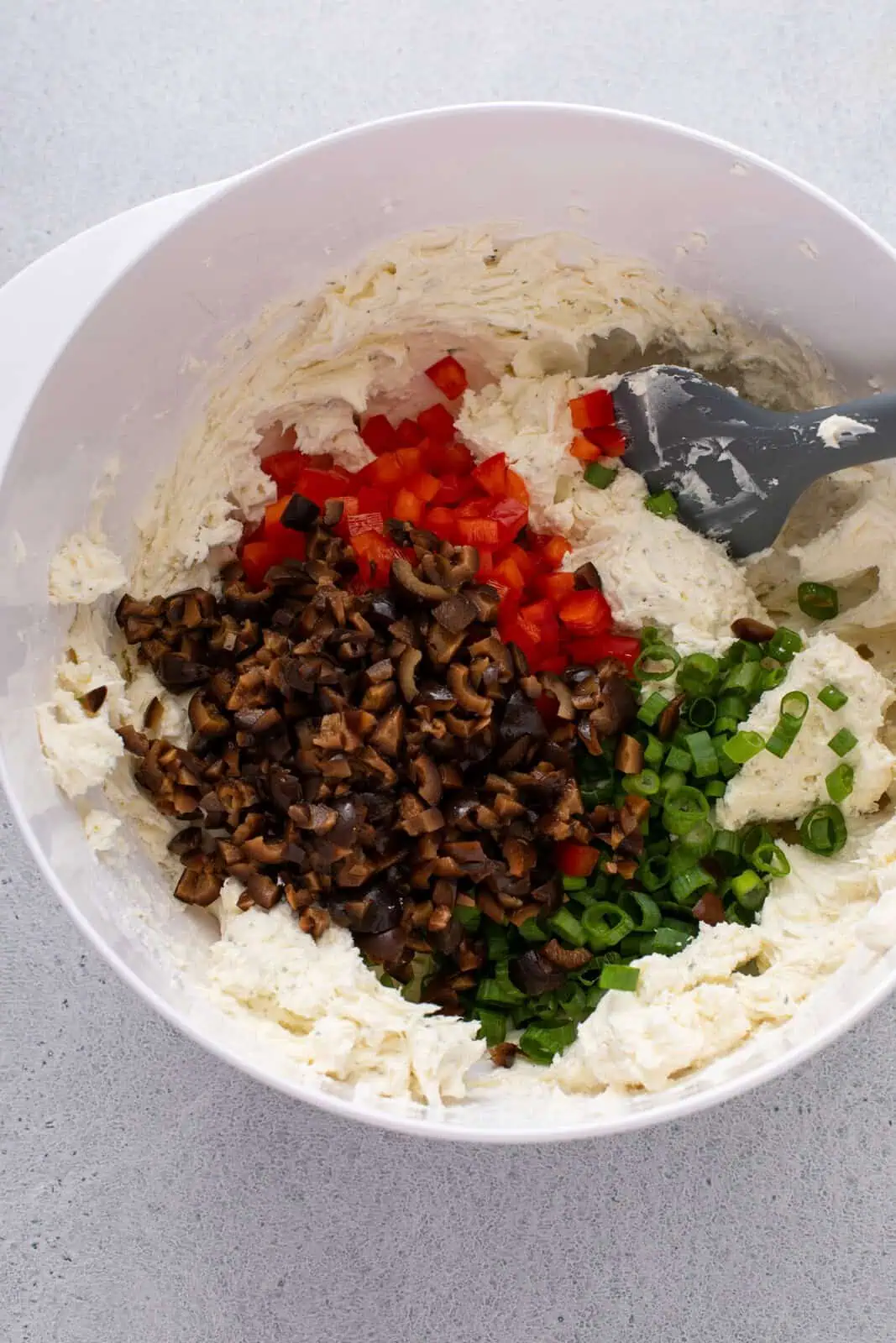 Adding vegetables to cream cheese in a bowl.