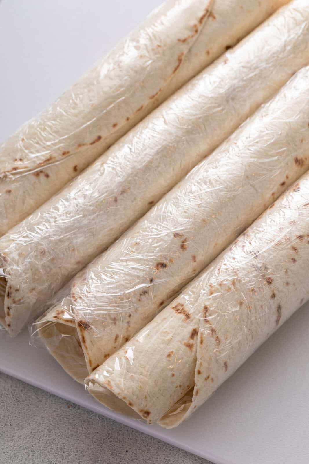 Four assembled cream cheese roll ups wrapped in plastic wrap.