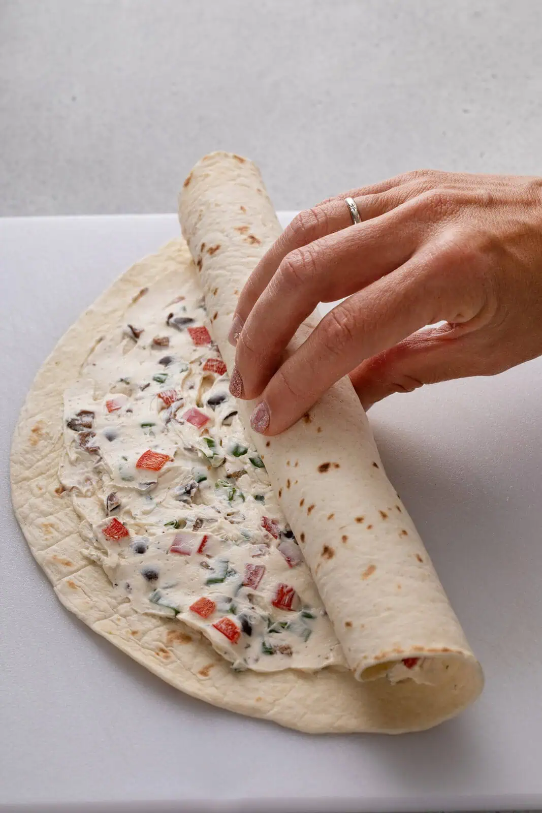 Tortilla being rolled around cream cheese filling.
