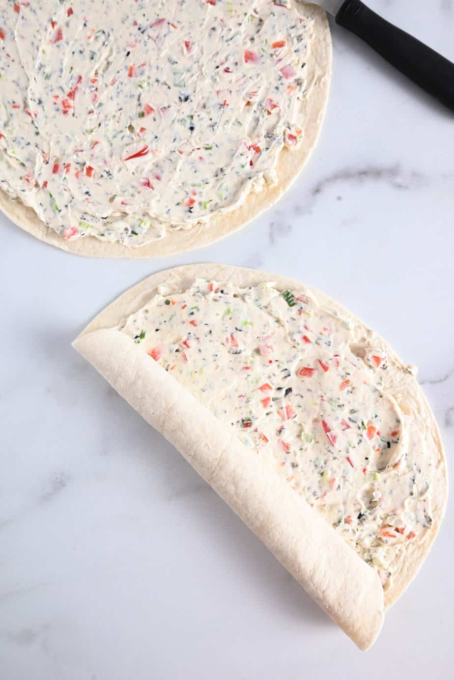 Flour tortillas spread with cream cheese filling being rolled up.