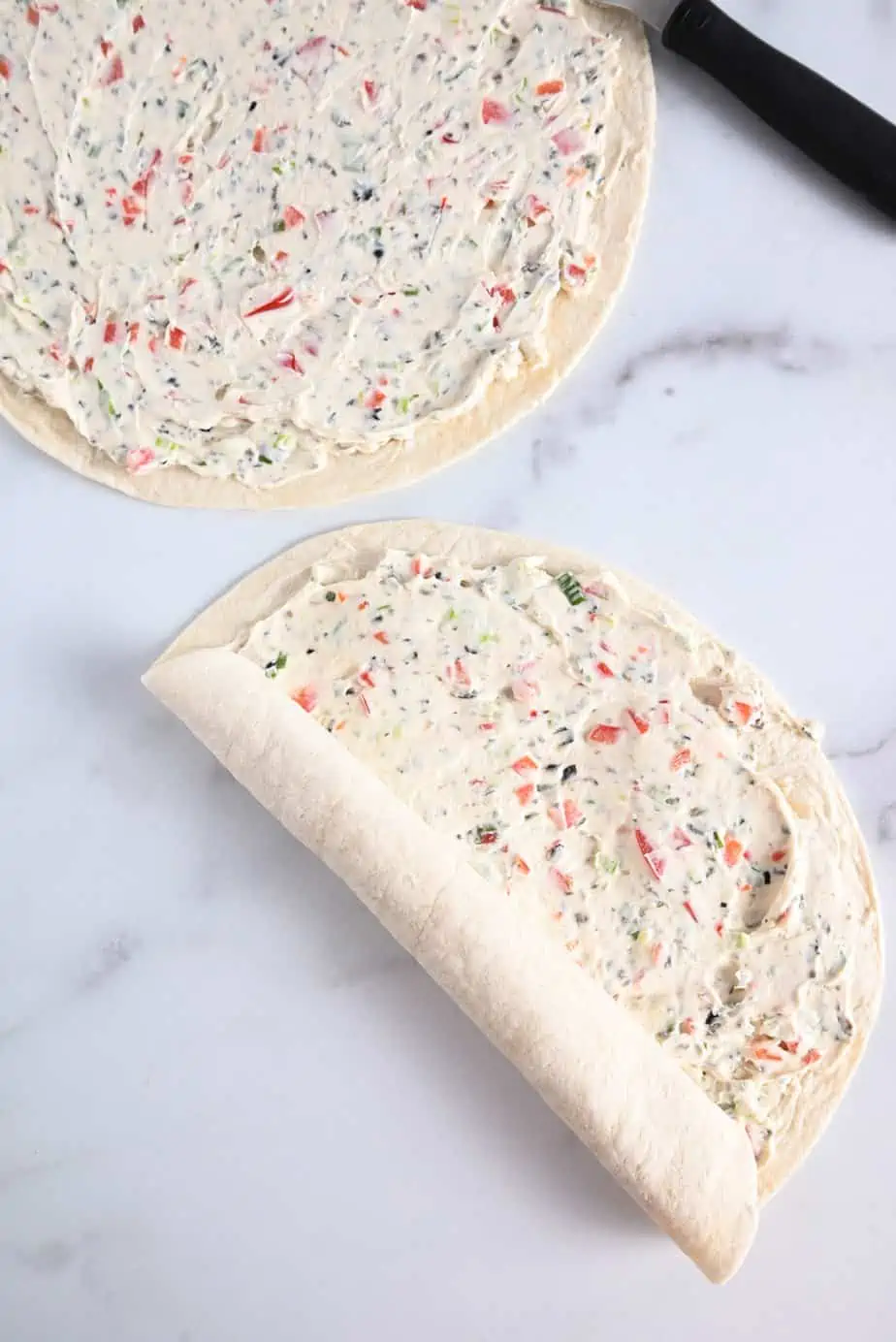 Flour tortillas spread with cream cheese filling being rolled up.