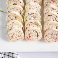 Cream cheese ranch roll ups arranged on a white platter, garnished with green onions.