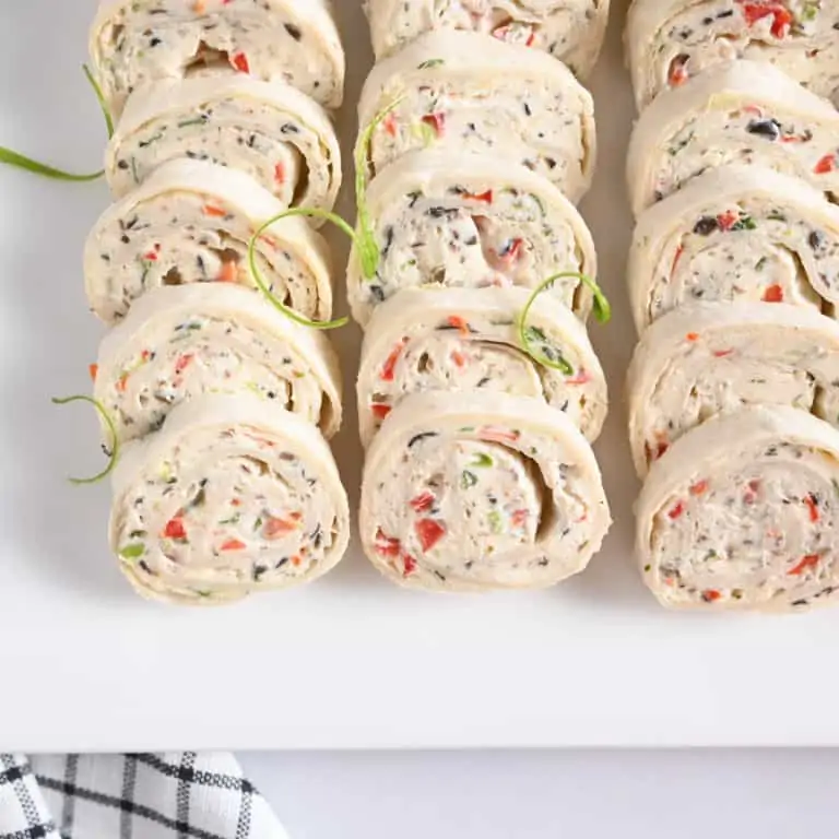 Cream cheese ranch roll ups arranged on a white platter, garnished with green onions.