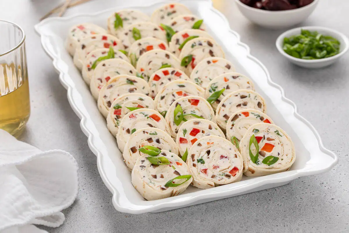 Sliced cream cheese ranch roll ups arranged in rows on a white platter.