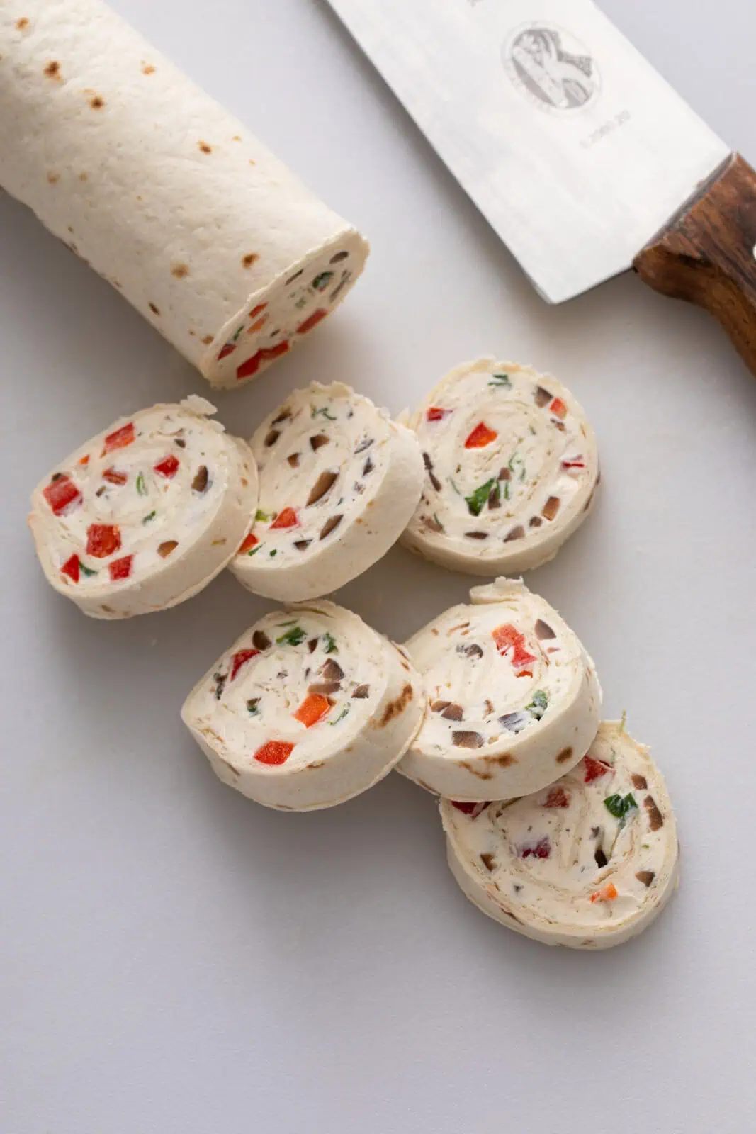 Cream cheese roll up being cut into slices on a cutting board.