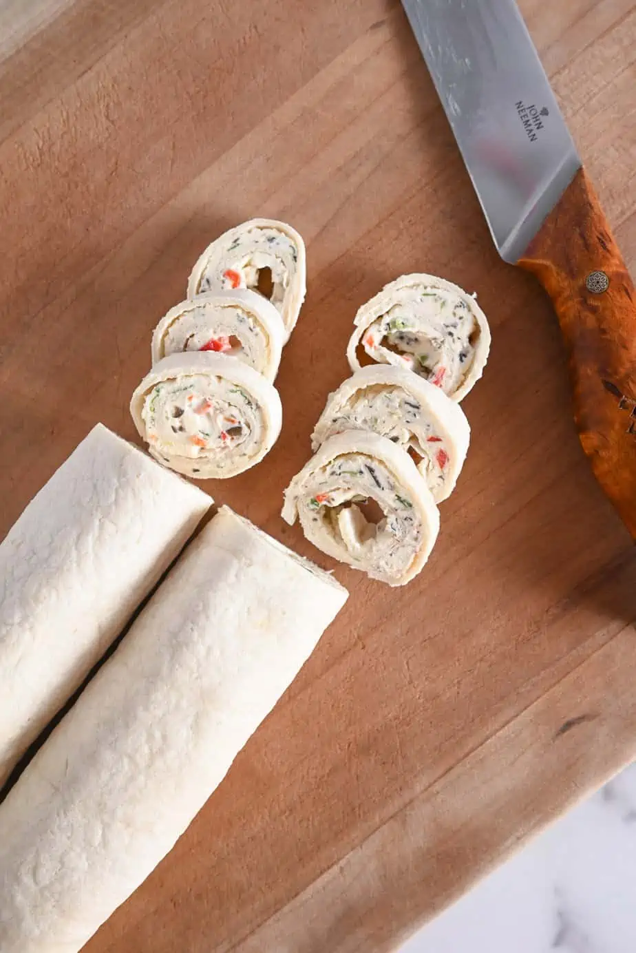 Cream cheese rollups being sliced on a wooden cutting board.