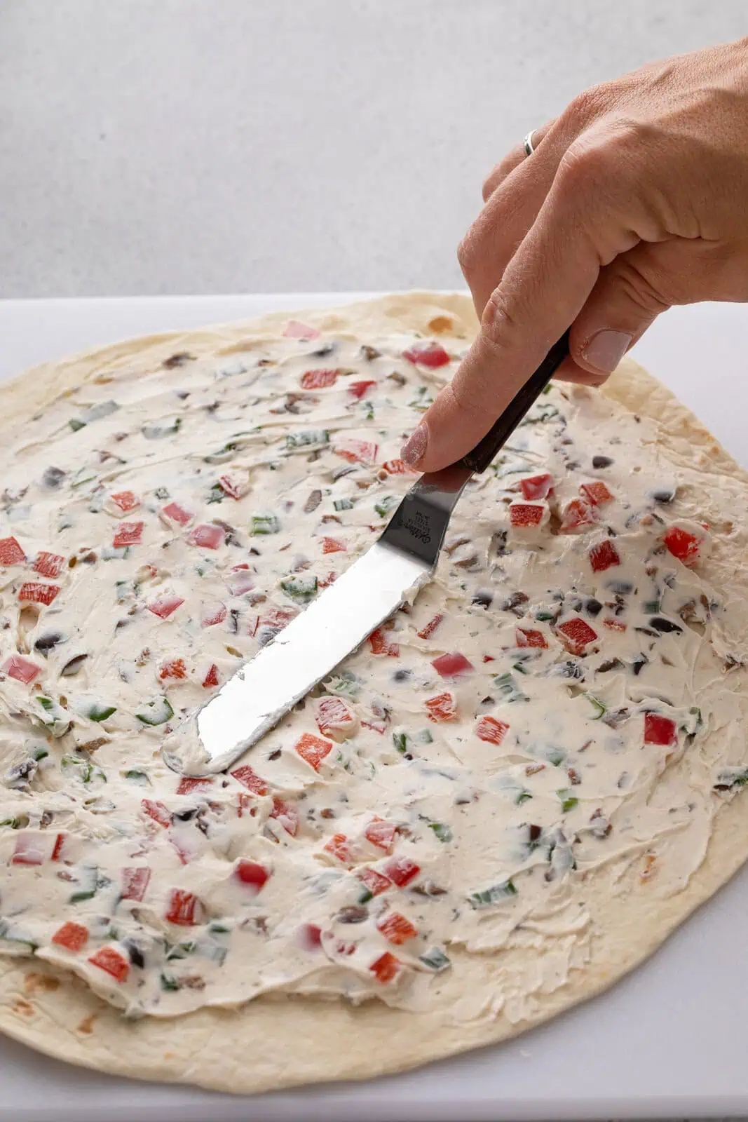 Cream cheese filling being spread over a large tortilla.