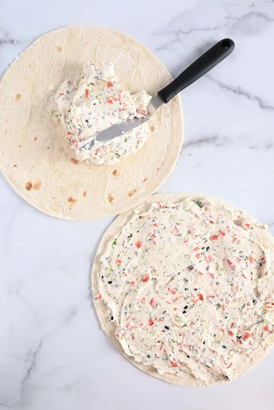 Cream cheese filling being spread onto tortillas with an offset spatula.