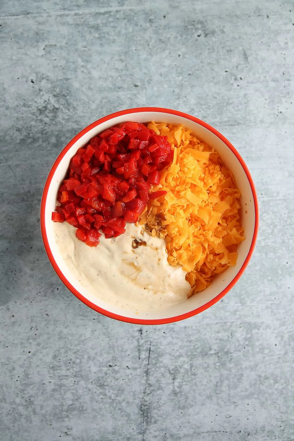 Overhead view of bowl with diced pimentos, shredded cheddar cheese and mayonnaise