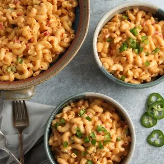 Large bowl of macaroni and pimento cheese alongside two serving bowls, forks and sliced jalapenos