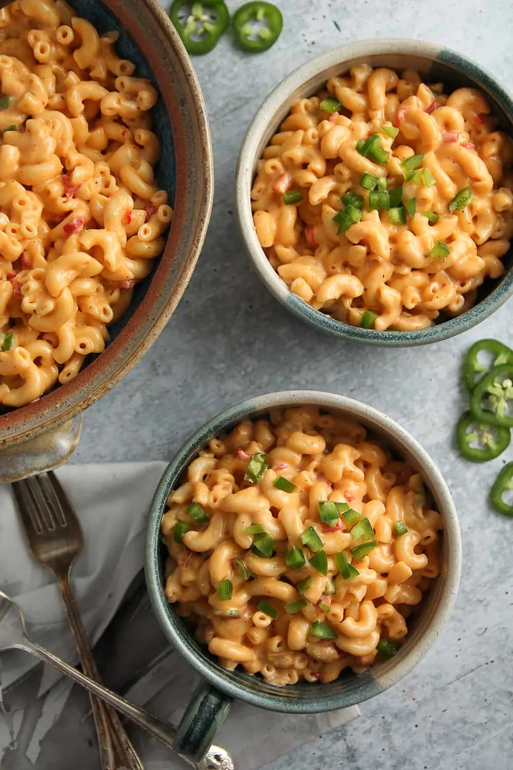 Green chili macaroni and pimento cheese in two serving bowls, garnished with diced jalapeno