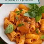 Close up of rigatoni tossed with roasted tomato sauce and garnished with basil in a white bowl. Text overlay includes recipe name.