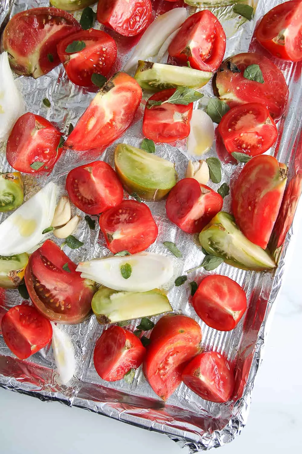 Fresh tomatoes and onions on a foil-lined sheet pan, ready to roast