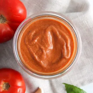 overhead view of roasted tomato sauce in a jar, next to fresh tomatoes