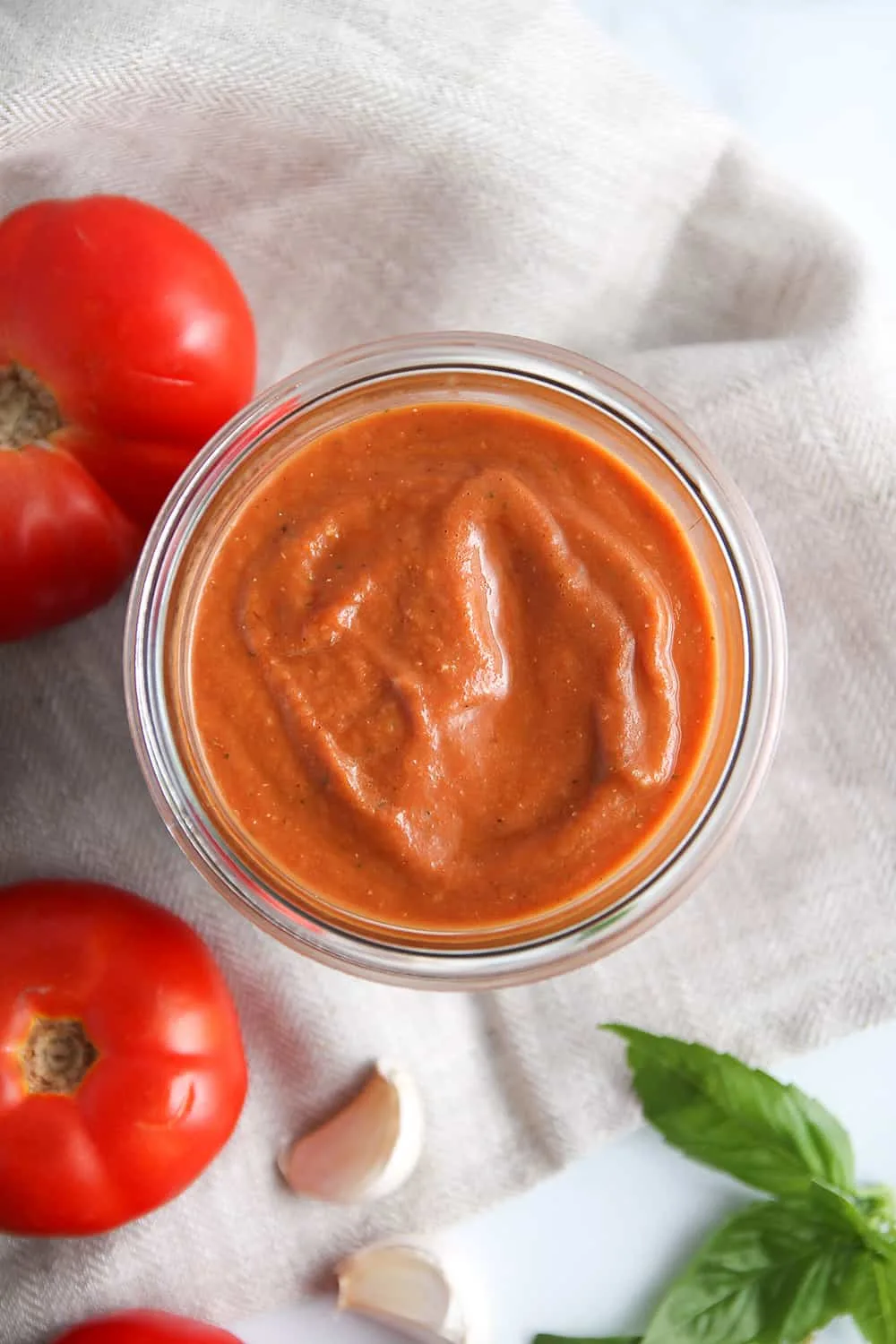 overhead view of roasted tomato sauce in a jar, next to fresh tomatoes