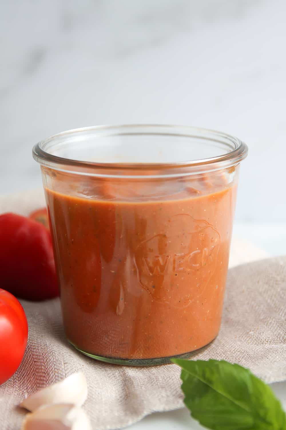 Homemade tomato sauce in a jar, with fresh tomatoes and herbs