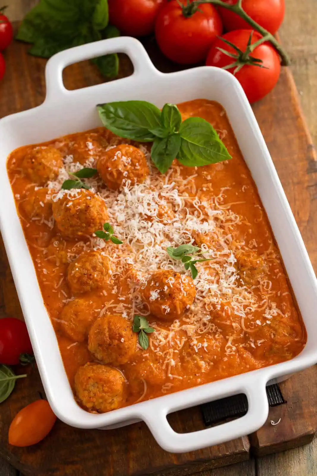Meatballs tossed with roasted tomato sauce and garnished with fresh basil in a white baking dish.