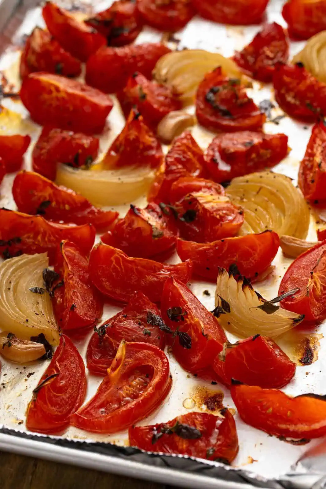 Roasted tomatoes, onions, and herbs on a sheet pan.