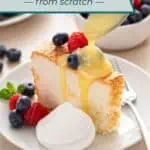 Lemon curd being drizzled over a slice of angel food cake on a white plate. The cake is also topped with fresh berries and set next to a dollop of whipped cream. Text overlay includes recipe name.
