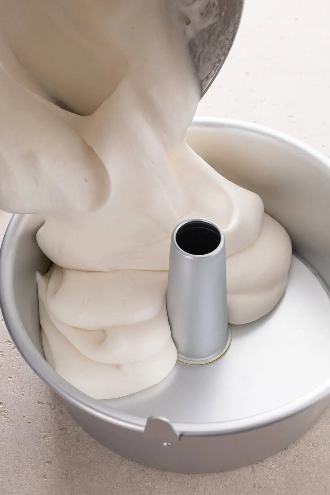 Angel food cake batter being poured into an aluminum angel food cake pan.
