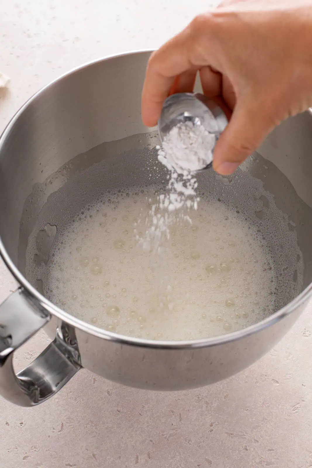 Person adding cream of tartar to foamy egg whites.