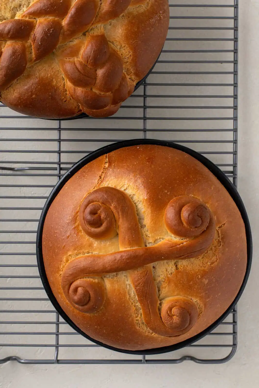 Baked paska loaves cooling in their pans on a wire rack.