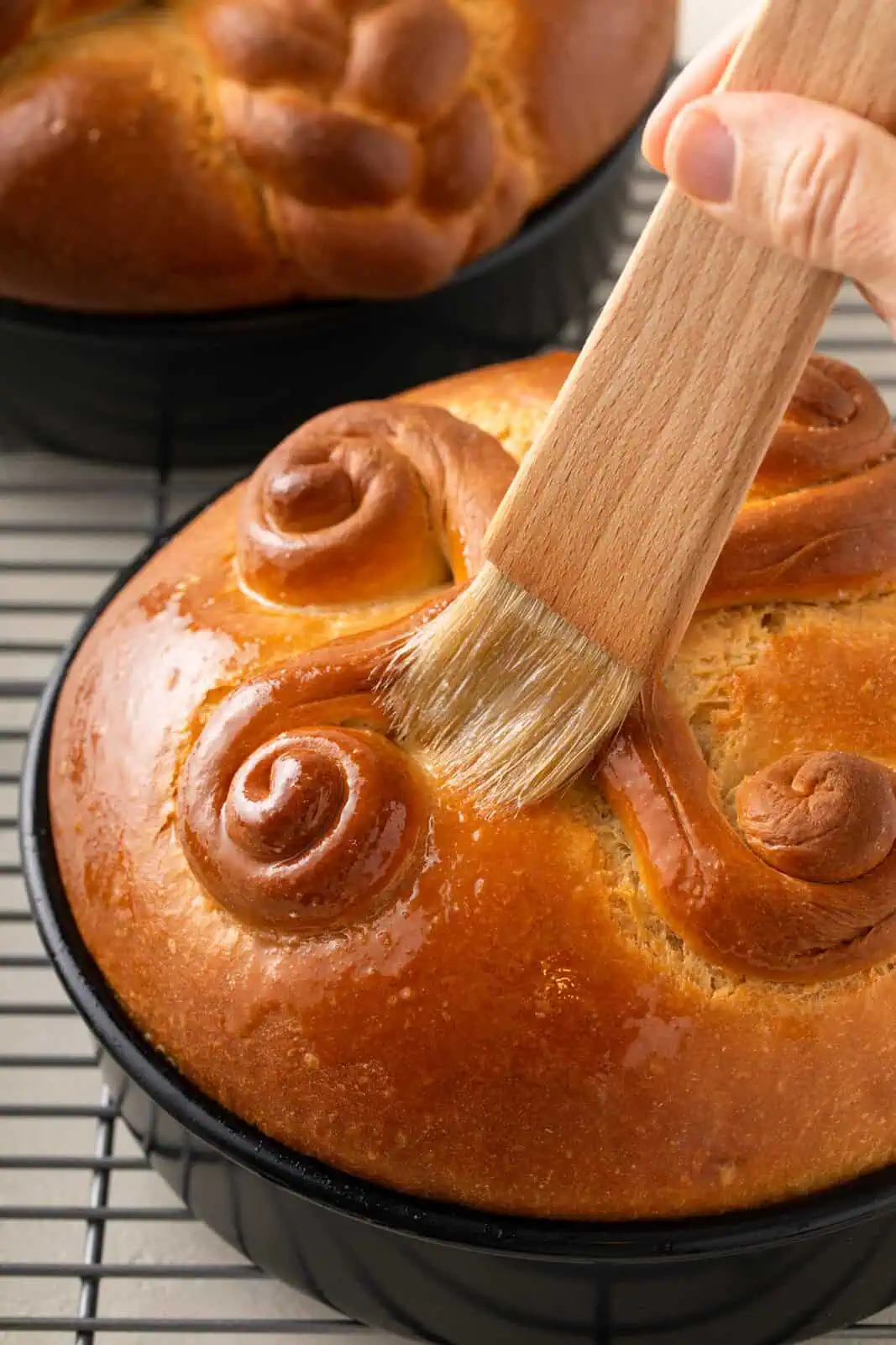 Melted butter being brushed over the top of baked paska loaves.