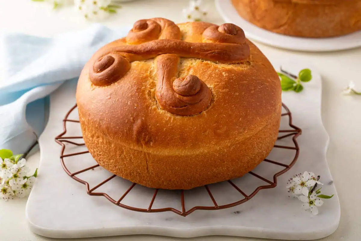 Cooled paska loaf decorated with swirls of dough set on a round wire rack.