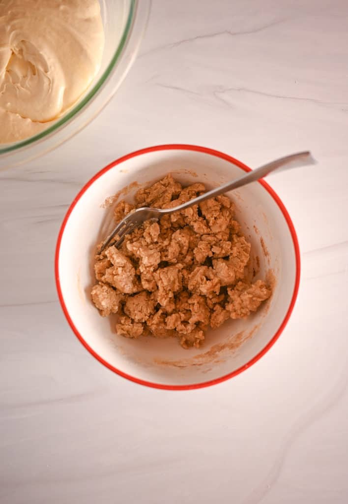 Cake mix crumbs being stirred with a fork in a white bowl with a red rim