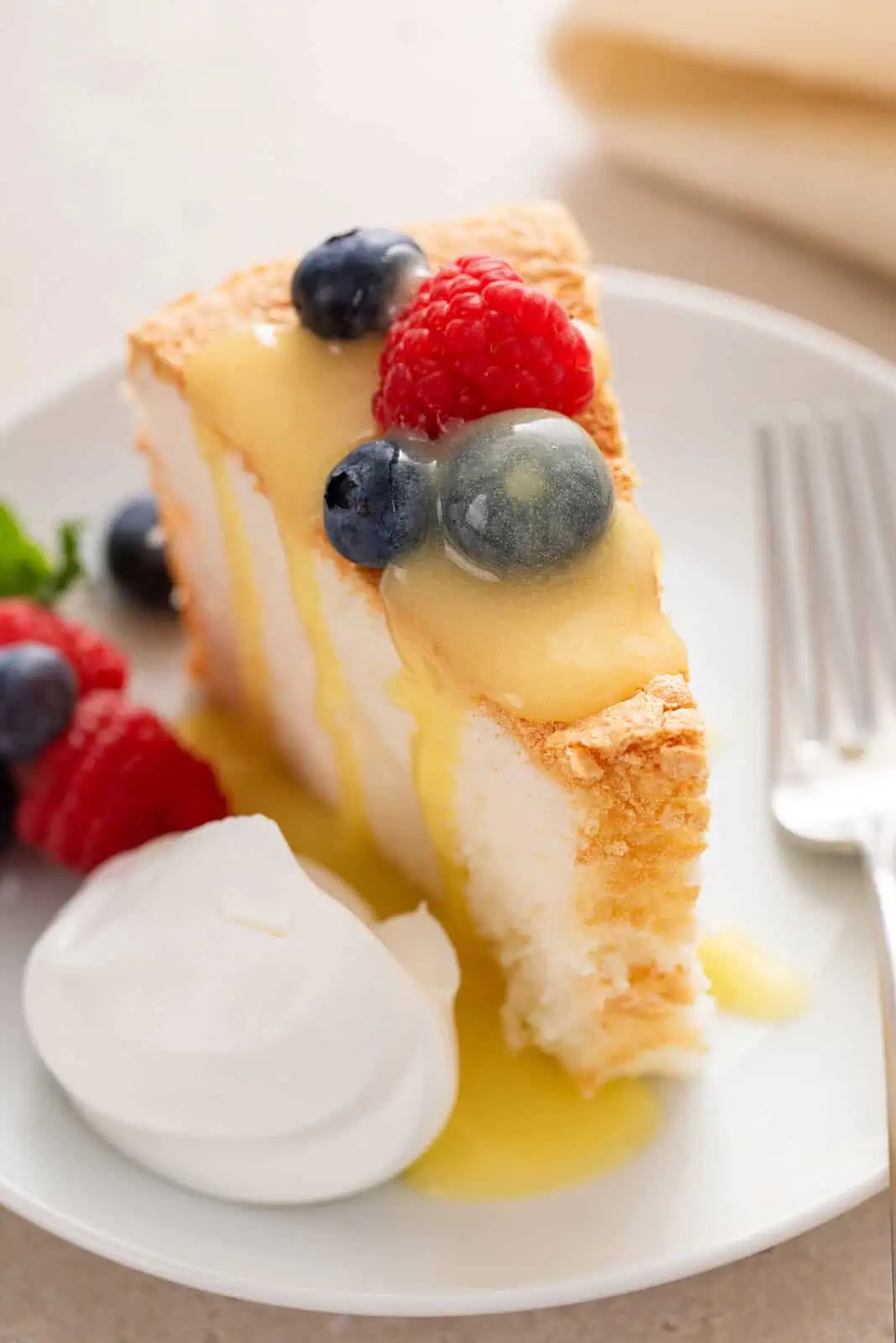 Angel food cake garnished with fresh berries, lemon curd, and a dollop of whipped cream on a white plate.