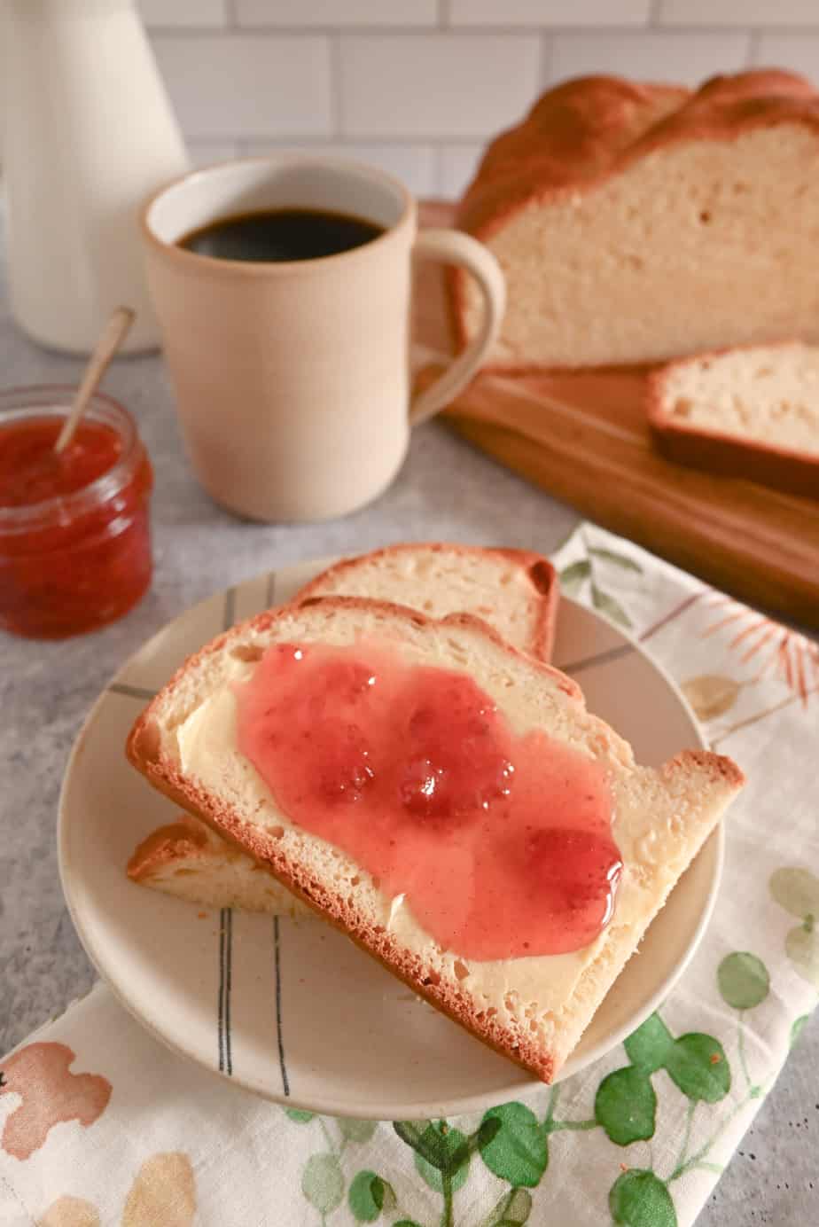 Slices of paska topped with butter and jam on a plate with coffee and the loaf of paska in the background
