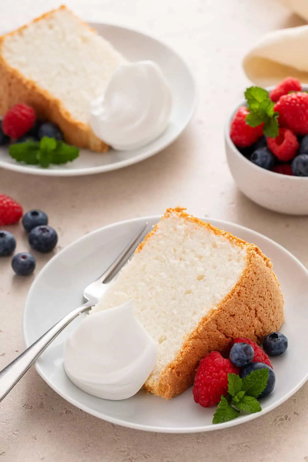 Two plated slices of angel food cake with whipped cream and fresh berries.