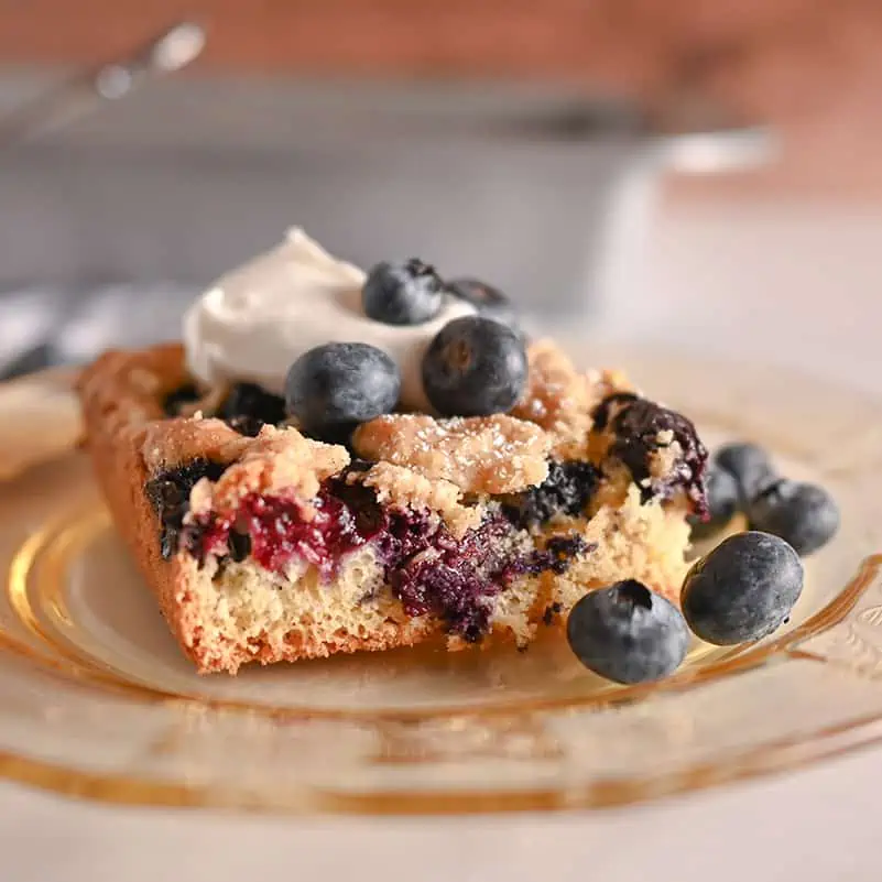 Slice of blueberry crumb cake topped with whipped cream and fresh blueberries