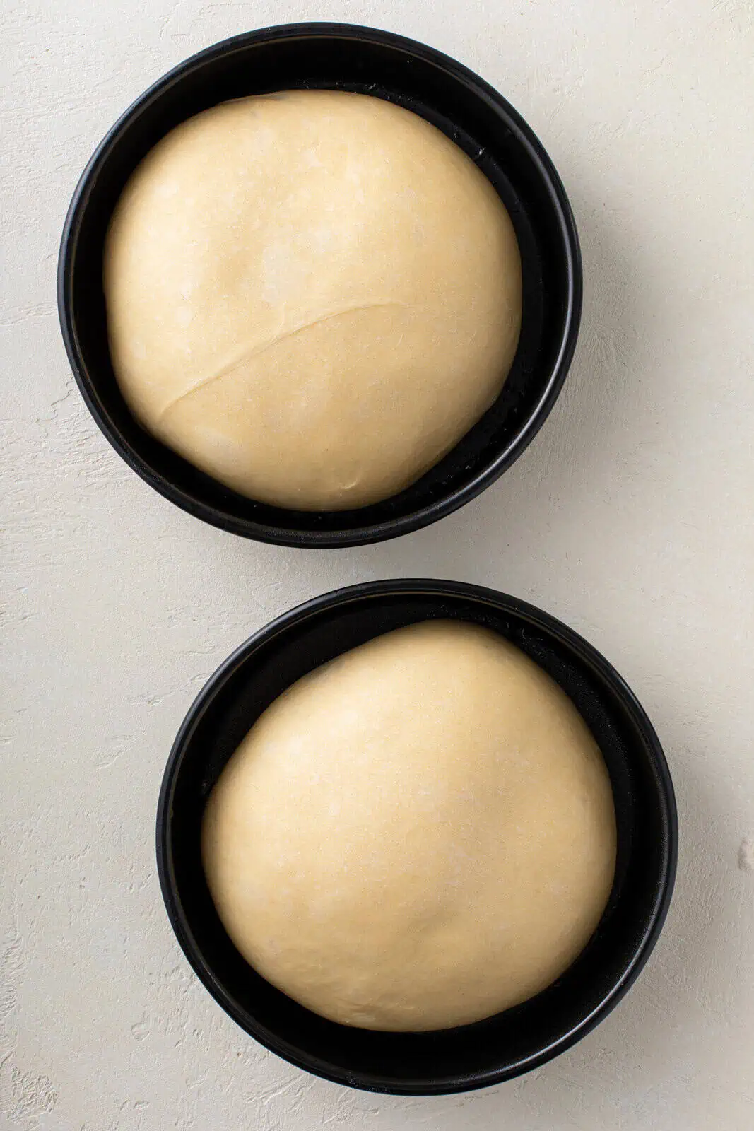 Paska dough shaped into two loaves in round cake pans, ready for their second rise.