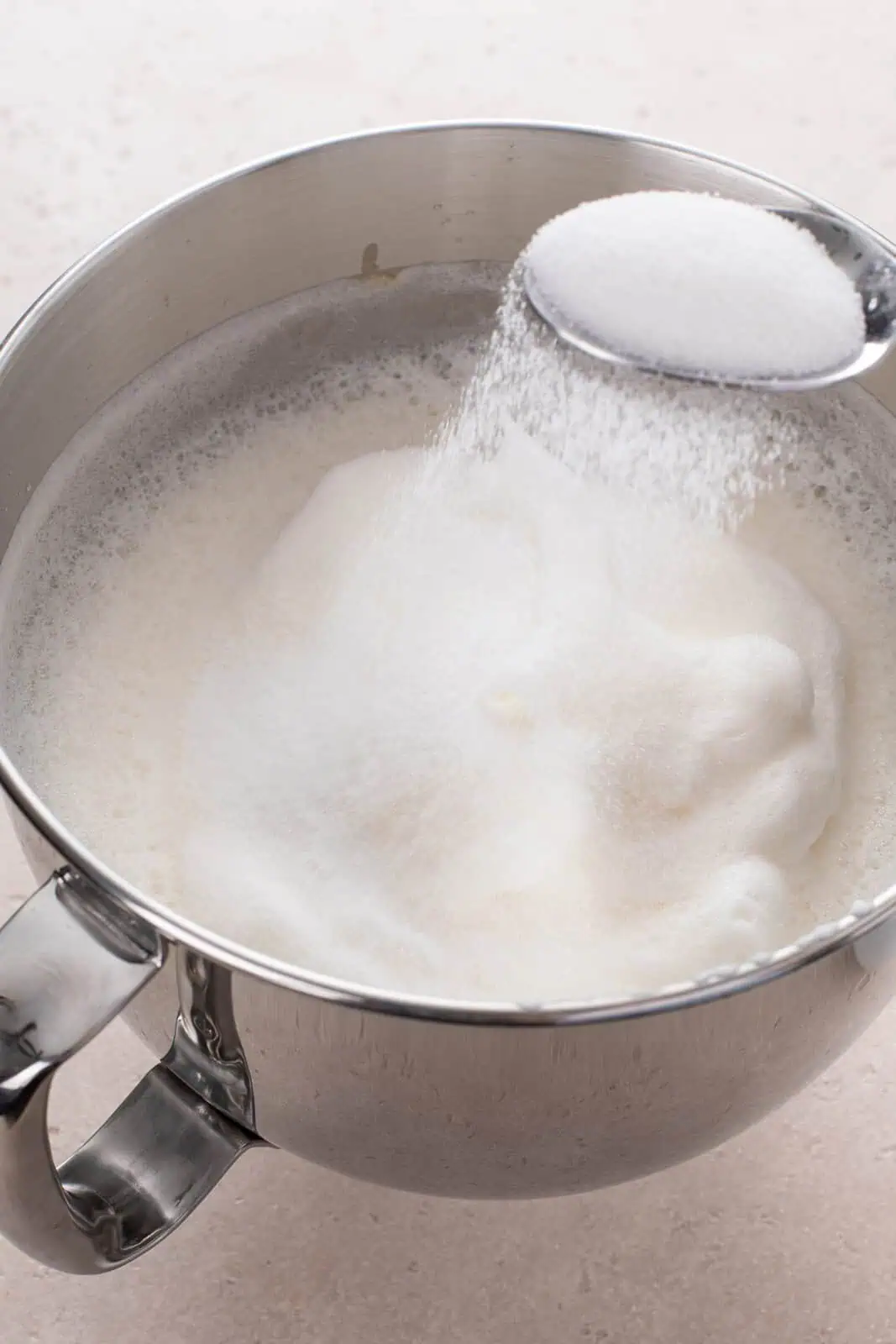Spoon sprinkling sugar over the top of beaten egg whites.