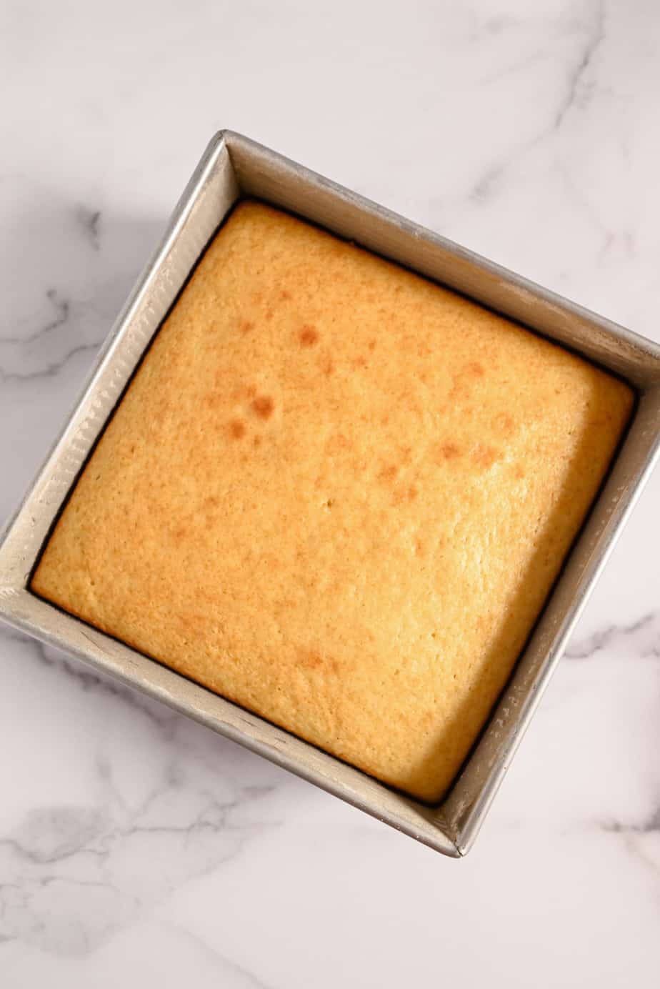 Baked homemade yellow cake in a cake pan, cooling on a marble countertop.