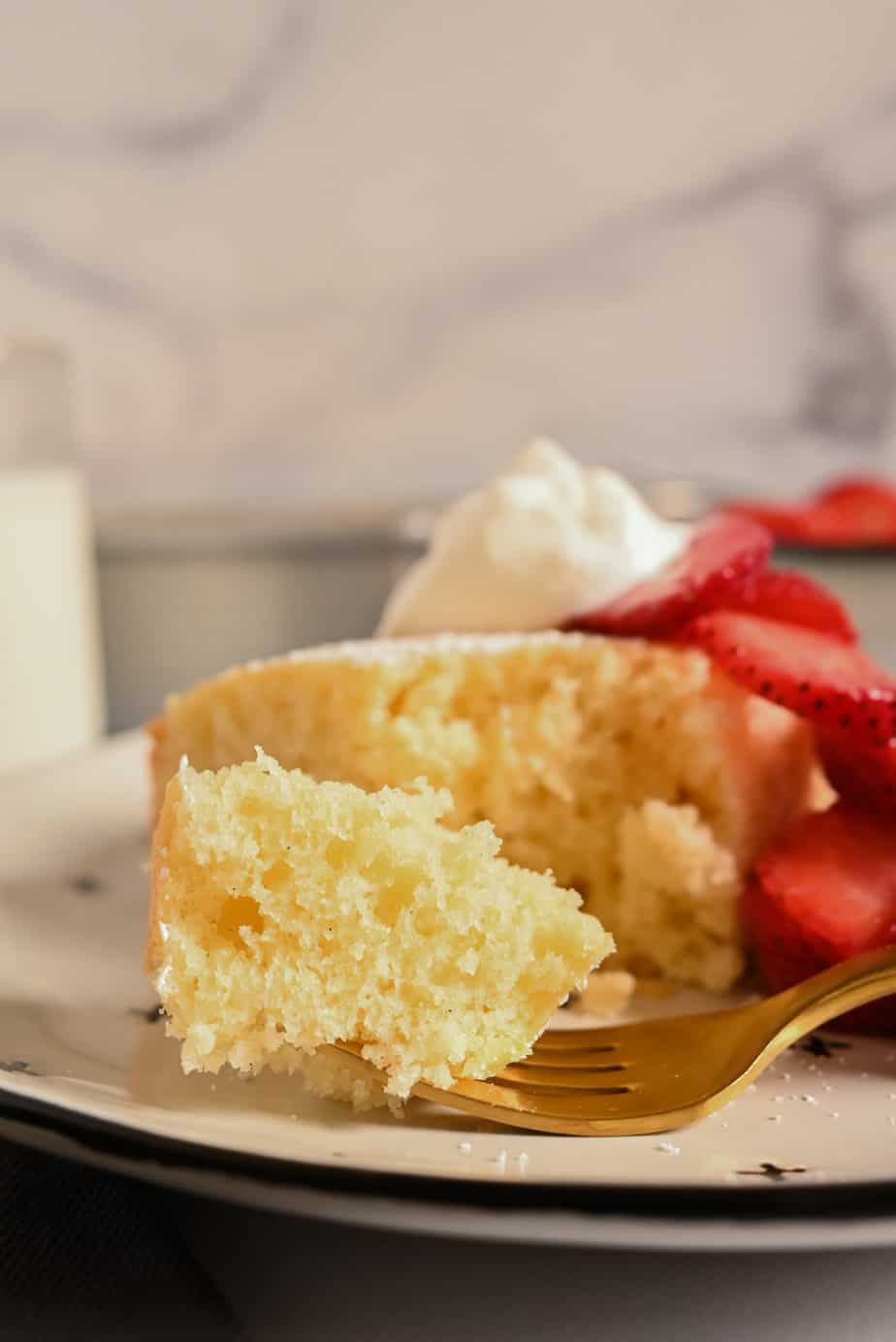 Close up of a bite of yellow cake on a golden fork, set on a plate.