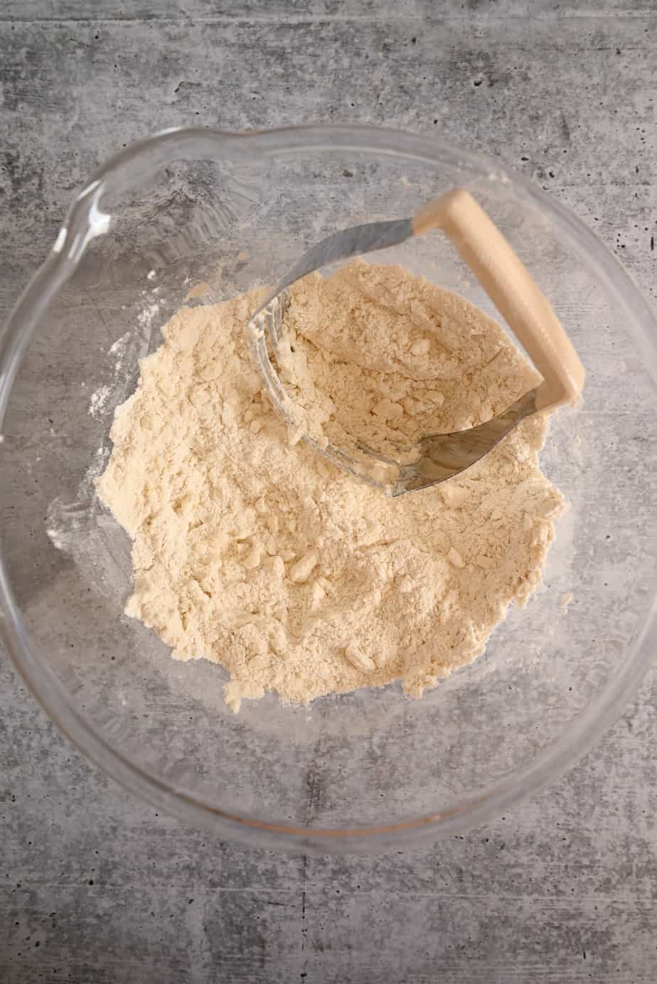 Pastry blender cutting butter into flour in a glass mixing bowl.