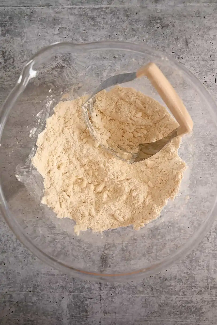 Pastry blender cutting butter into flour in a glass mixing bowl.