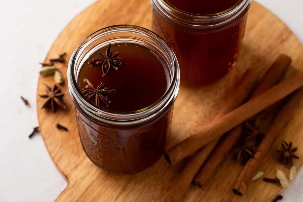 Overhead view of homemade chai concentrate in a glass jar, surrounded by whole spices.