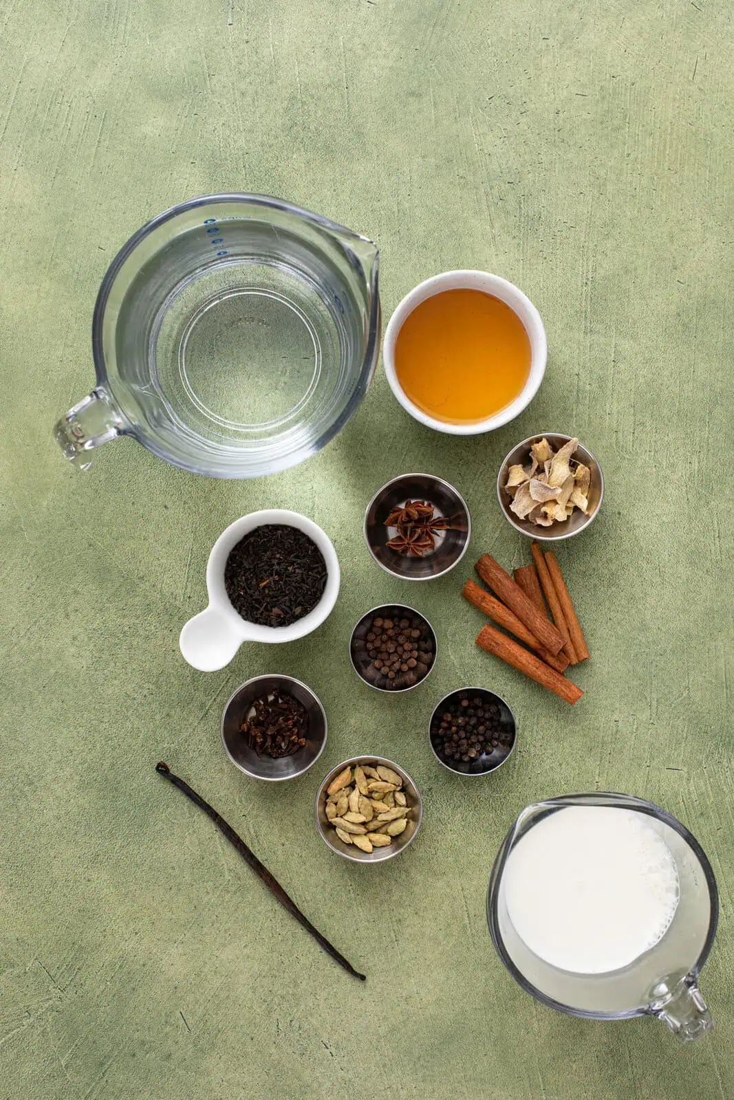 Ingredients for homemade chai concentrate arranged on a green countertop.