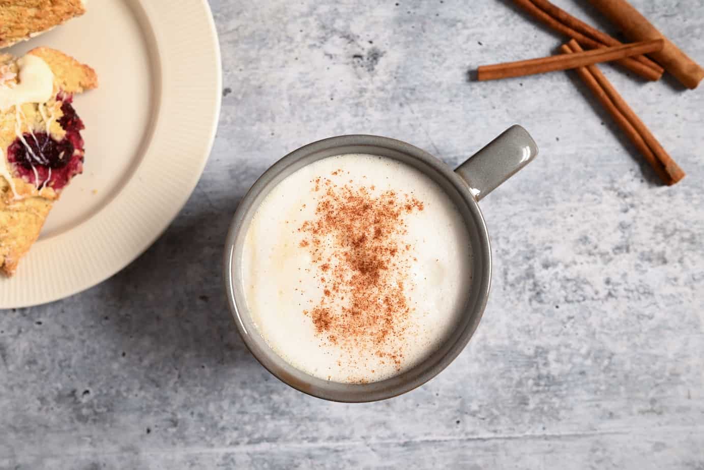 Overhead view of a mug filled with a chai latte next to a white plate of scones